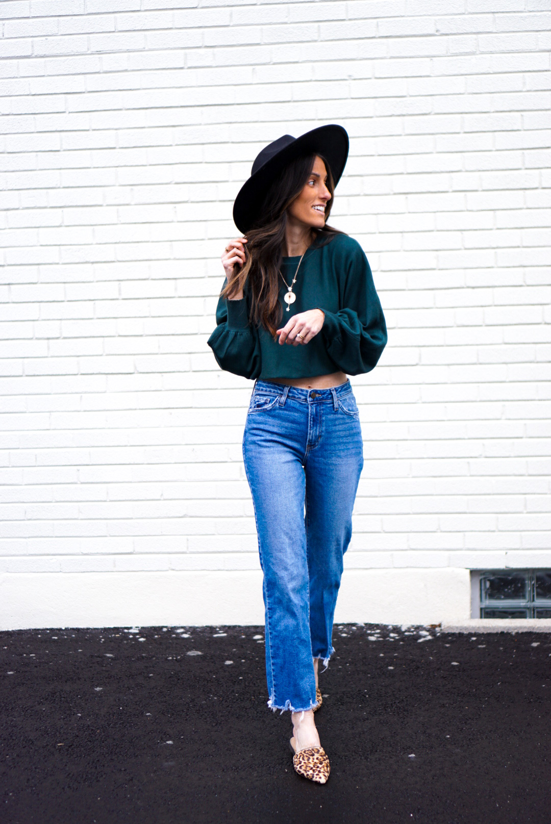 Woman wearing cropped sweater with high waisted mom jeans, wide brim hat, and leopard mules